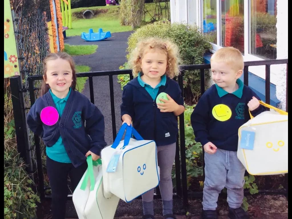 Three school children carrying play bags outside